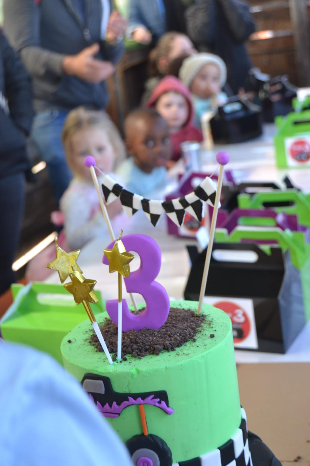 Green monster-truck birthday cake with a number 3, children seated behind it