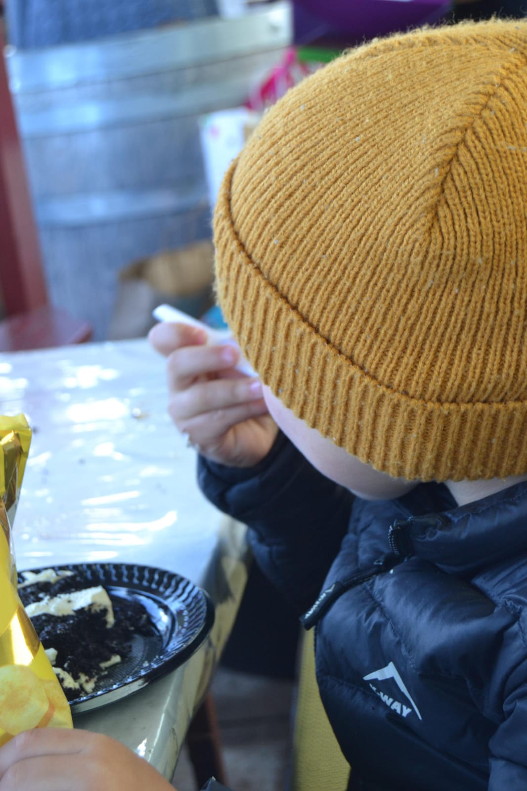 Child in a mustard beanie eating cake at a party table