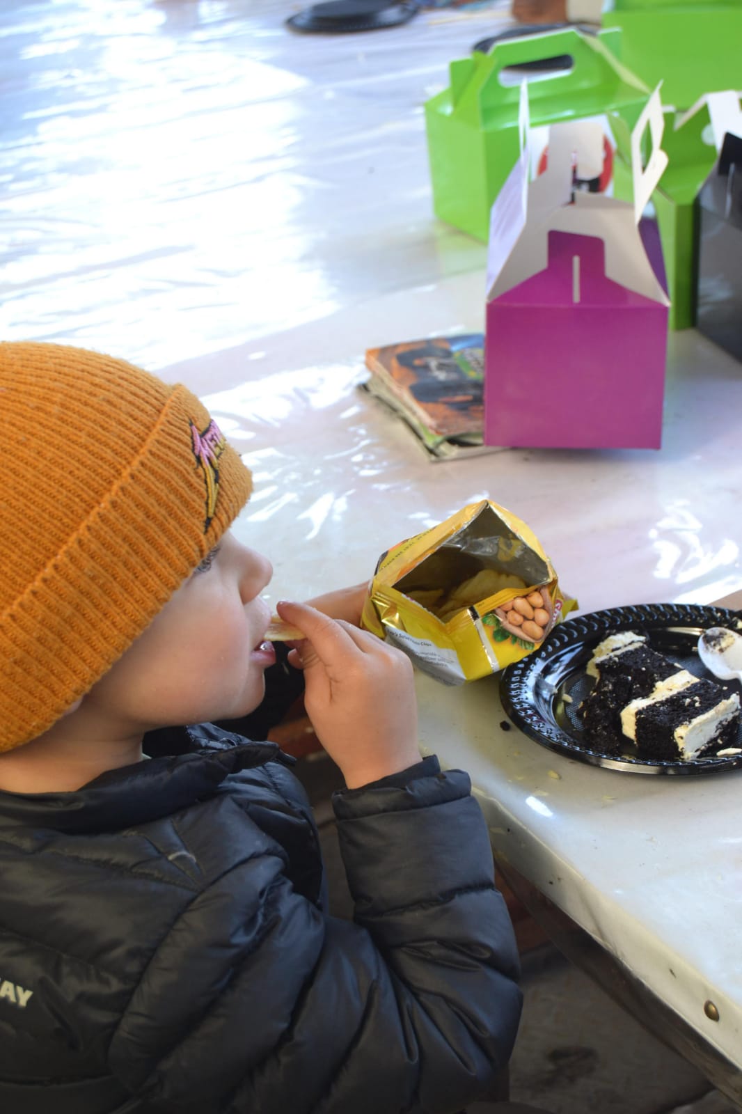 Child in a mustard beanie eating a snack beside a slice of cake
