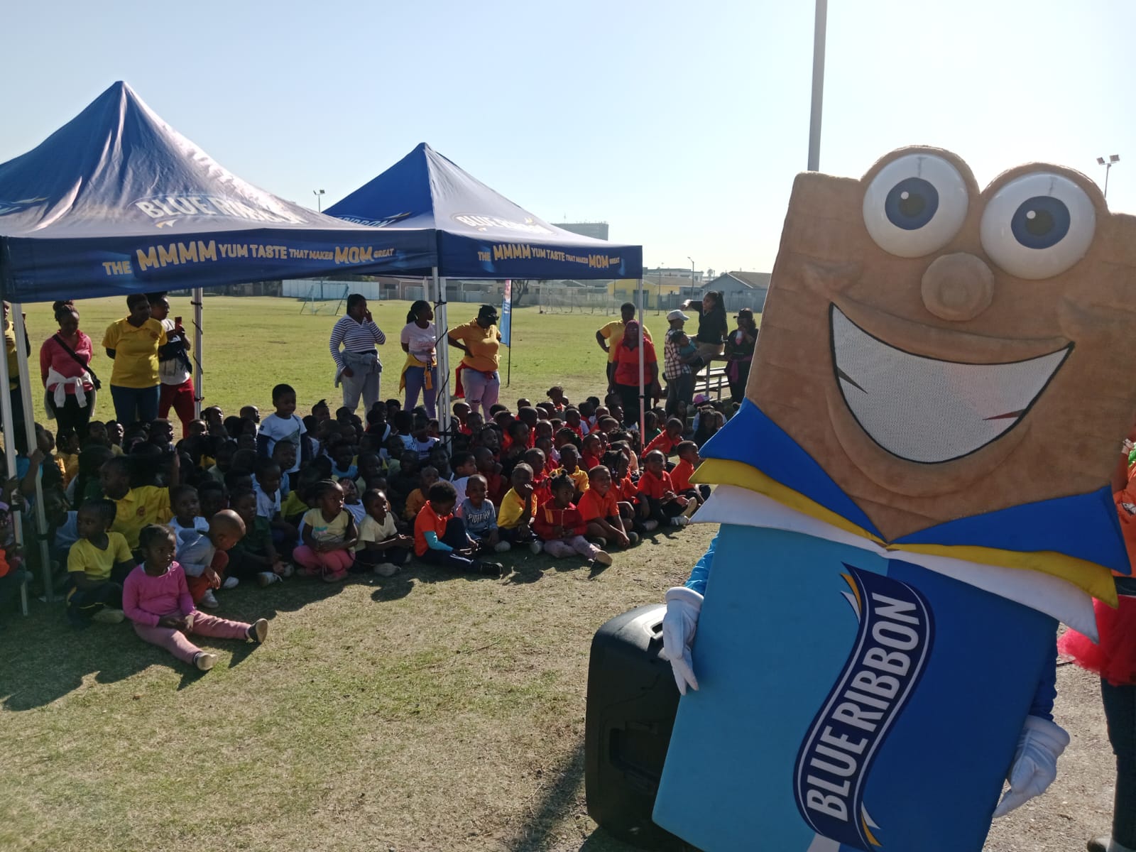 Children seated on a sports field beside a mascot